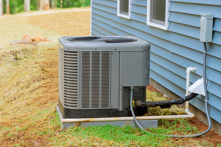 Central AC unit installed on the outside of a blue house in a grass yard 