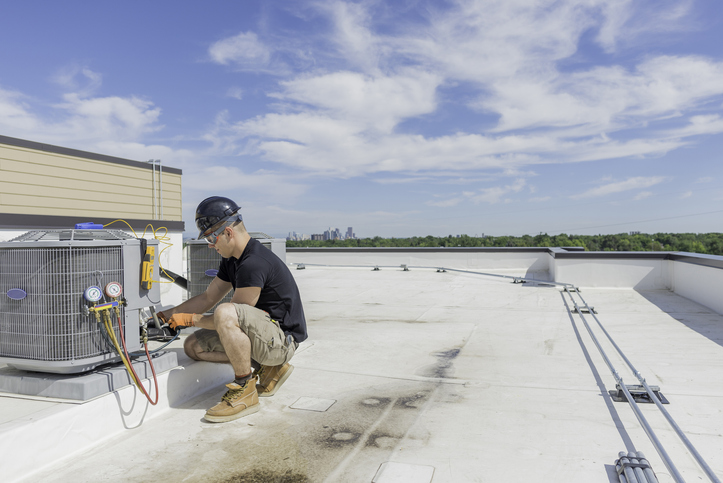 technician checking air conditioning unit outside commercial building