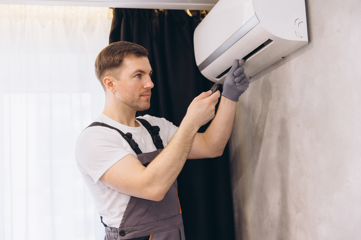 Repair person in gray uniform repairing an air conditioning unit with a screwdriver, ensuring optimal performance and comfort in the home.