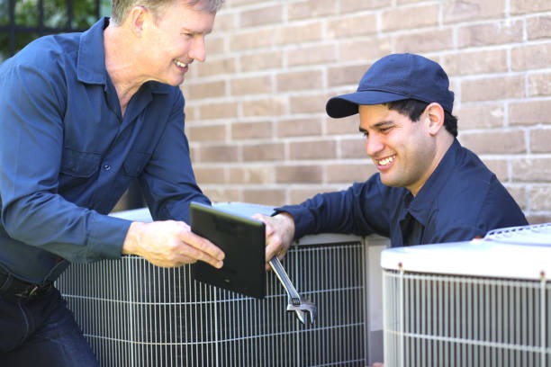 2 technicians outside in between 2 acs smiling talking to one another 