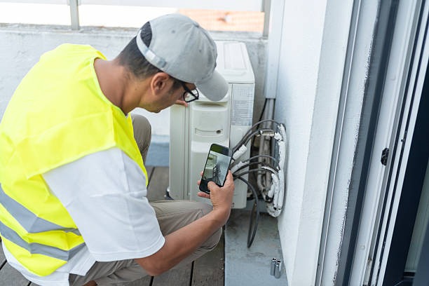 hvac repair technician in high res vest taking a picture of part of a cooling system with iphone