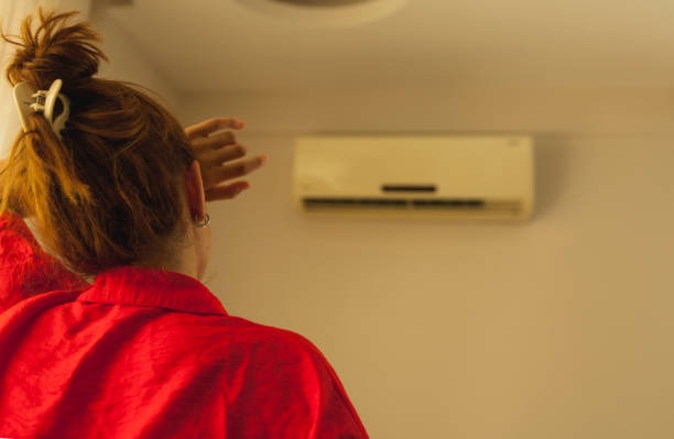 woman with hair up looking at the ac inside that is not working