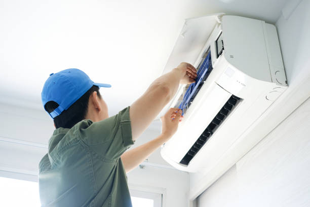 man in blue hat fixing air conditioning unit