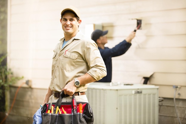 technician in khaki outfit smiling and holding bag of tools