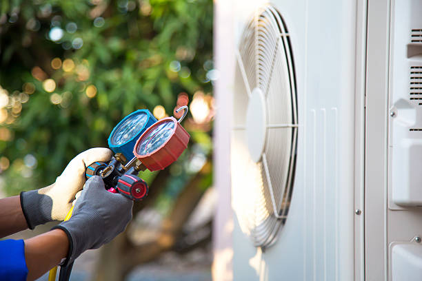 Mechanic air conditioner technician using manifold gauge checking refrigerant for filling home air conditioning and air duct cleaning and maintenance outdoor compressor unit.