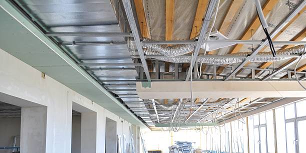 View of an unfinished interior space showcasing metal framing, insulation, ventilation pipes, and electrical wiring for a suspended ceiling